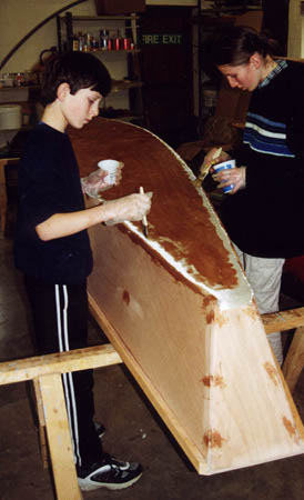 Children epoxy coating a canoe they have built